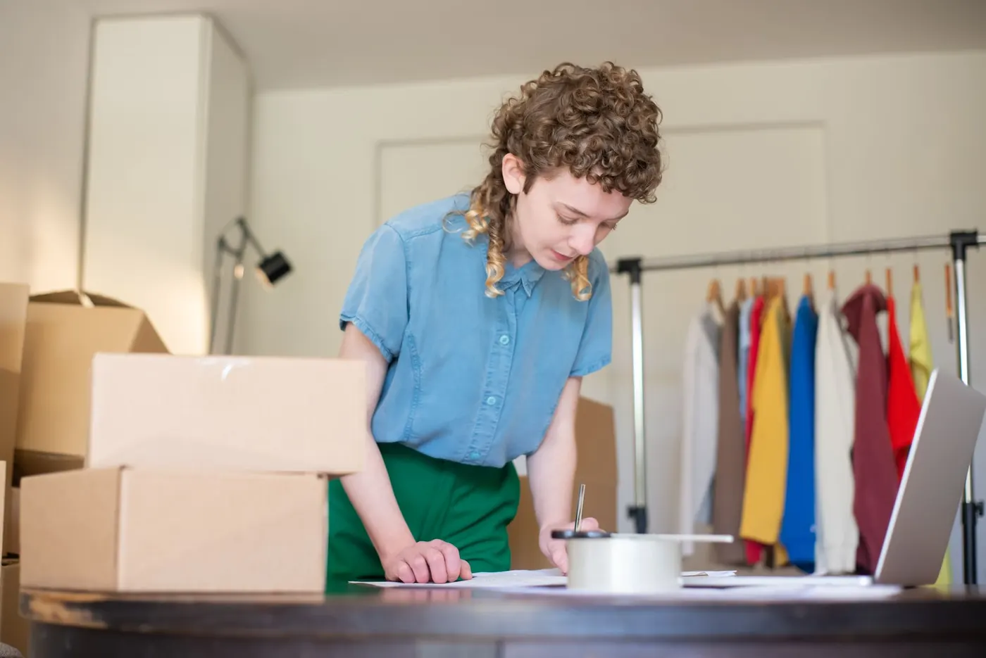 Small shop owner preparing orders next to boxes and a clothing rail